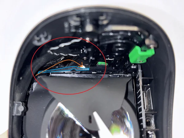 Reference image showing blue-marked plastic piece and orange arrow for cable routing